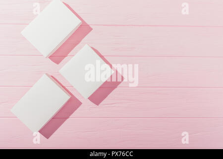 Flat lay side frame of rhombus blank presents. Top view three empty white gift boxes on pink wooden table. Stock Photo