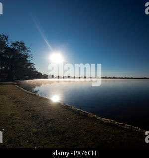 Bright morning sun in a blue sky with reflections in water Stock Photo