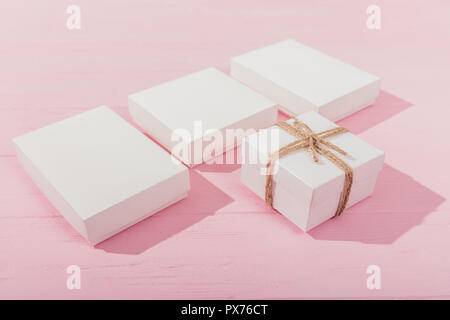 Close-up gift boxes on pink wooden table. Set of white presents for celebration. Stock Photo