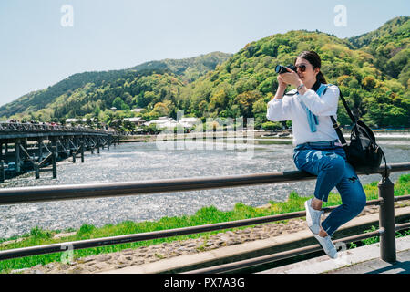 elegant photographer sitting on the handrail and taking picture of the Togetsukyo bridge. traveling lens man hobby love taking scenery photo by slr ca Stock Photo