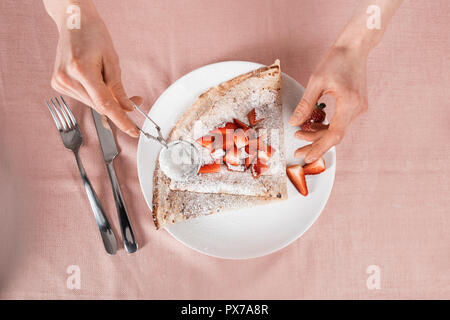 above view of female hands that are spreading powdered sugar on a crepe Stock Photo