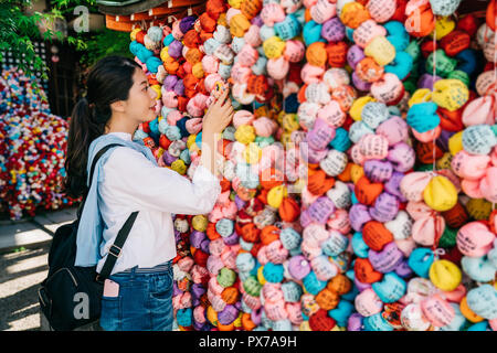 pretty tourist visiting temple and hanging her wish dolls on the wish wall in Japan. traditional blessing culture in Kongoji. Japanese young lady grac Stock Photo