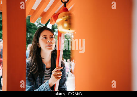 attractive female traveler experience the Japanese culture, pulling the rope to make the bell rings. Japanese lady blessing in peaceful temple. Japane Stock Photo