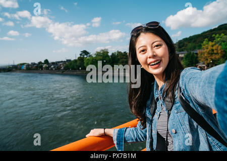 elegant asian traveler taking selfie on the bridge with the clean river. Asian beautiful girl smiling happy on Uji bridge vacation enjoying warm sunsh Stock Photo