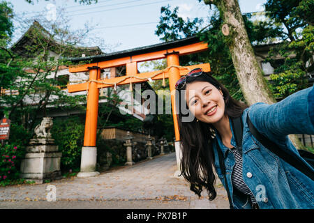 elegant traveler putting fashion sunglasses on her head and taking selfie with Torii. backpacker vacation selfie happy lady smiling taking photo with  Stock Photo