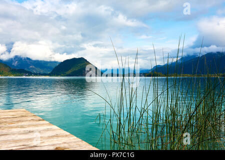 Lake Wolfgagsee in Austria near Salzburg with pier and water grass, with mountains in background under blue sky with clouds Stock Photo