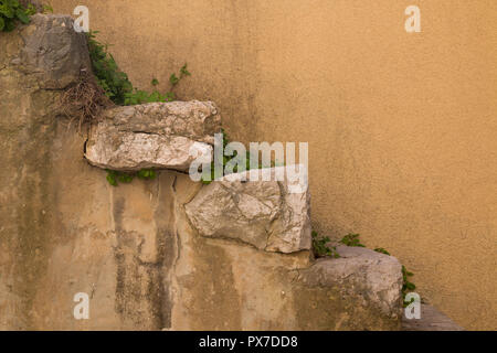 Wall of a building with a light orange facade and stairs made of big natural pieces of a stone. Plants among the stones. Historical city Vrbnik, islan Stock Photo