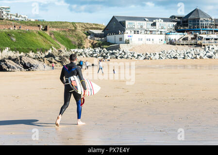 A surfer carrying his surfboard walking on Fistral Beach in Newquay in Cornwall. Stock Photo