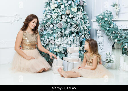 Mom and daughter sitting under the Christmas tree near the boxes with gifts. Stock Photo