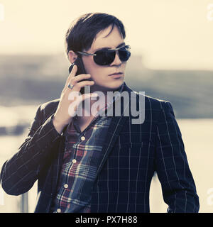 Young business man in sunglasses using smart phone walking in city street Stock Photo