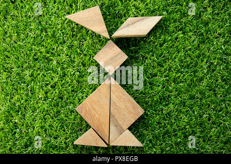 Wooden tangram puzzle in rabbit shape on artificial green grass background (Concept of Happy Easter) Stock Photo