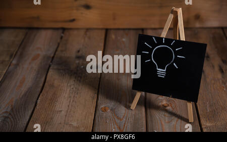 Idea concept. Light bulb drawn on a chalkboard, dark wooden background, copy space Stock Photo