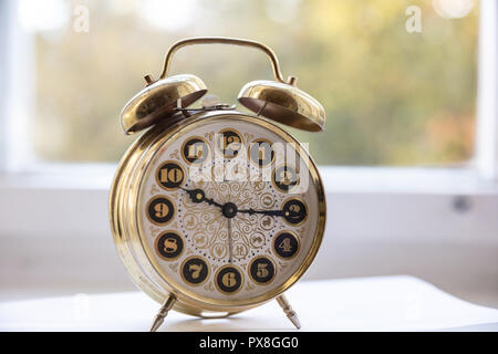 Time management. Golden alarm clock in the morning, blur glass window background, Stock Photo