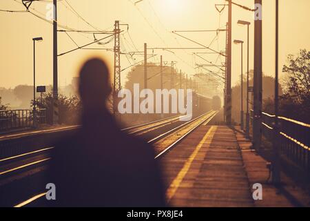 Silhouette of man waiting at railroad station platform at sunrise. Stock Photo