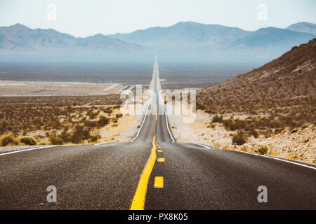 Classic panorama view of an endless straight road running through the barren scenery of the American Southwest with extreme heat haze in summer Stock Photo