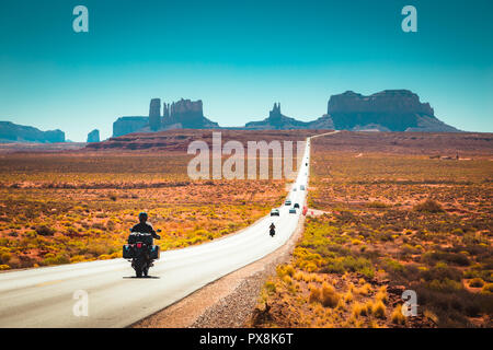 Classic panorama view of motorcyclist on historic U.S. Route 163 running through famous Monument Valley in beautiful golden evening light at sunset in Stock Photo
