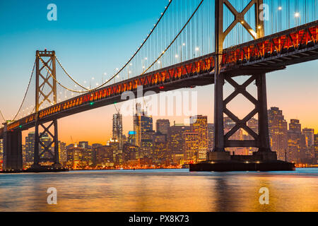 Classic panoramic view of San Francisco skyline with famous Oakland Bay Bridge illuminated in beautiful golden evening light at sunset in summer, San  Stock Photo