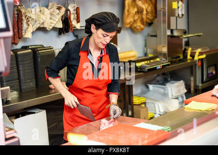 Female butcher cutting meat at counter in butchery with a ax Stock Photo