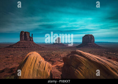 Classic panoramic view of scenic Monument Valley with the famous Mittens and Merrick Butte illuminated in beautiful mystic moonlight on a starry night Stock Photo