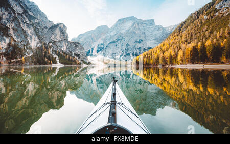 Beautiful view of kayak on a calm lake with amazing reflections of mountain peaks and trees with yellow autumn foliage in fall, Lago di Braies, Italy
