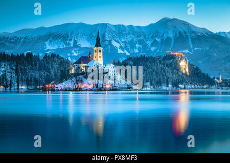 Beautiful twilight view of Lake Bled with famous Bled Island and historic Bled Castle in the background during scenic blue hour at dawn in winter, Slo Stock Photo