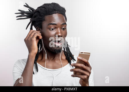 African man wearing headphones and holding his smartphone against white background Stock Photo