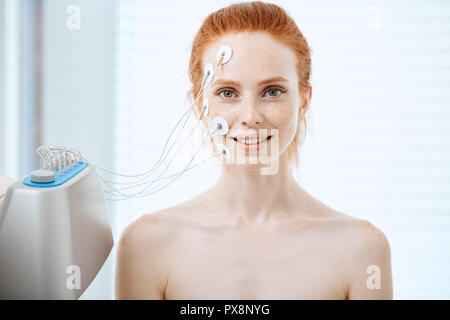 Young woman with electrodes on her face, receiving electric stimulation. Stock Photo