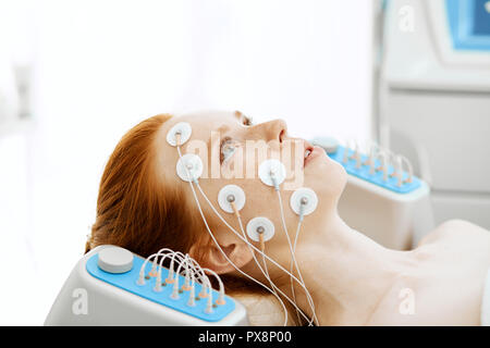 Young woman with electrodes on her face, receiving electric stimulation. Stock Photo