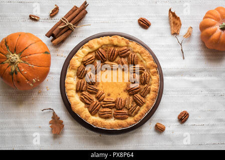 Pumpkin and Pecan Pie with cinnamon on white linen background, top view, copy space. Homemade autumn pastry for Thanksgiving. Stock Photo