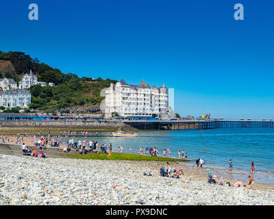 26 July 2018: Llandudno, Conwy, UK - Llandudno beach on a hot summer day, and the Grand Hotel. In the foreground is the pebble sea defence. Stock Photo