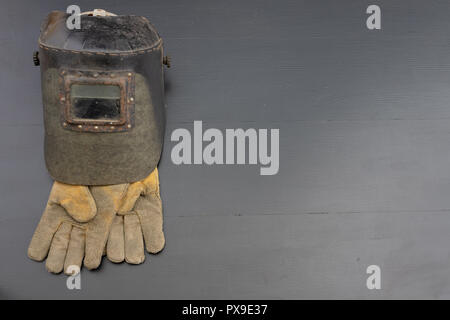Welder's mask and gloves on a black workshop table. Protective clothing for workers in metalware. Dark background. Stock Photo