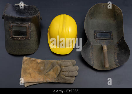 Welder's mask and gloves on a black workshop table. Protective clothing for workers in metalware. Dark background. Stock Photo