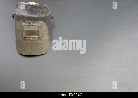 Welder's mask and gloves on a black workshop table. Protective clothing for workers in metalware. Dark background. Stock Photo