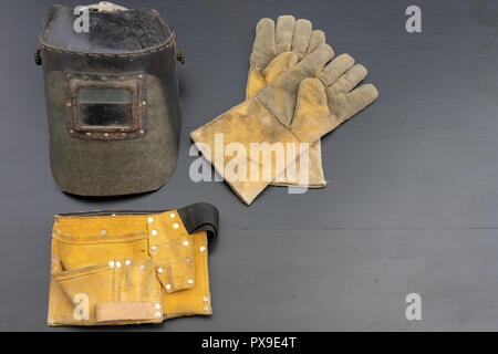 Welder's mask and gloves on a black workshop table. Protective clothing for workers in metalware. Dark background. Stock Photo