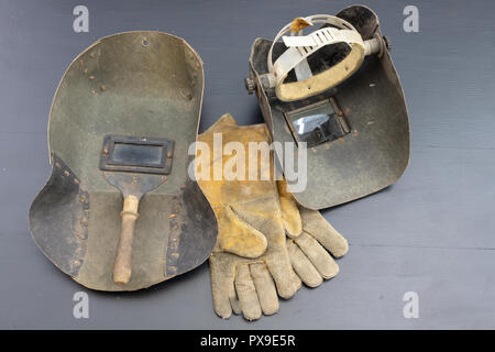 Welder's mask and gloves on a black workshop table. Protective clothing for workers in metalware. Dark background. Stock Photo