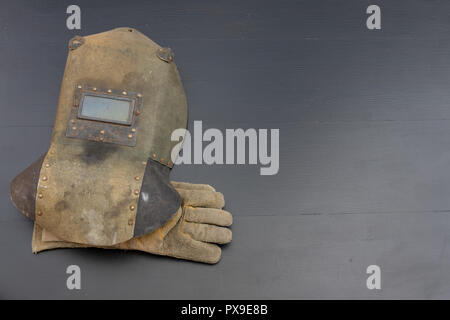 Welder's mask and gloves on a black workshop table. Protective clothing for workers in metalware. Dark background. Stock Photo