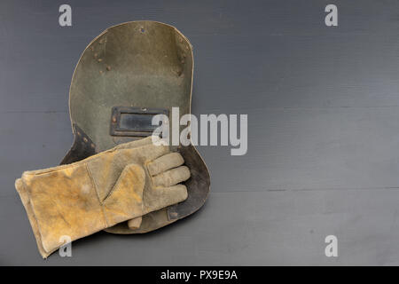 Welder's mask and gloves on a black workshop table. Protective clothing for workers in metalware. Dark background. Stock Photo