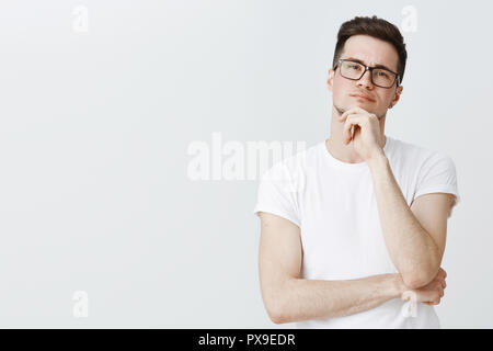 Waist-up shot of creative male photographer looking at model thoughtful holding hand on chin as thinkings making decision standing focused and serious standing against gray background determined Stock Photo