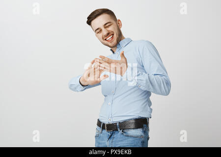 Yeah I am billionaire. Delighted stylish and successful young businessman in blue shirt with cool haircut smiling broadly rubbing palms as if throwing cash or money at camera being rich and happy Stock Photo