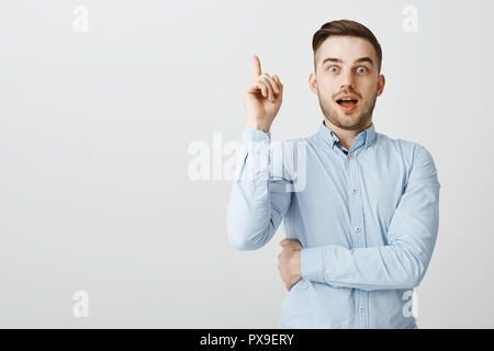 Guy got excellent idea sharing with team. Enthusiastic excited good-looking male in formal blue shirt raising index finger in eureka gesture holding breath and opening mouth while adding suggestion Stock Photo