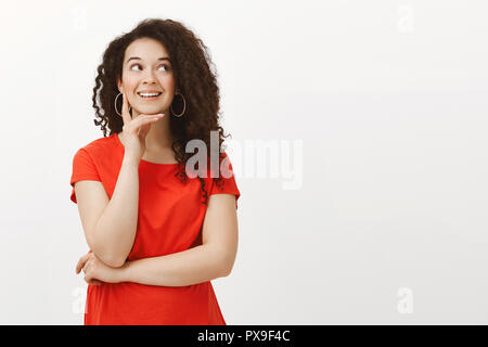 https://l450v.alamy.com/450v/px9f4c/portrait-of-dreamy-good-looking-stylish-girlfriend-with-curly-hair-in-red-dress-smiling-joyfully-while-looking-aside-holding-hand-on-chin-dreaming-or-imaging-curious-things-thinking-over-gray-wall-px9f4c.jpg