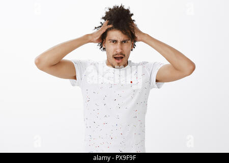 Guy feeling offended hearing girlfriend wants cut his hair. Portrait of displeased unhappy and gloomy handsome eastern man with curly hairstyle, touching head and frowning with dislike at camera Stock Photo