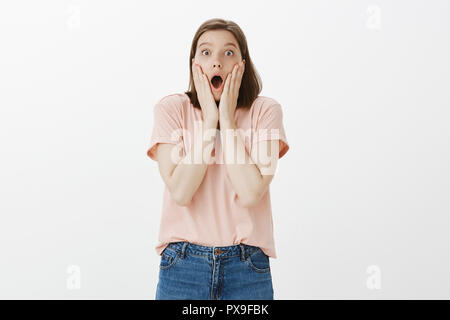 Girl received unbelievable present, dropping jaw from amazement. Woman stands over gray background, gasping, saying wow holding palms near opened mouth while being surprised and astonished Stock Photo