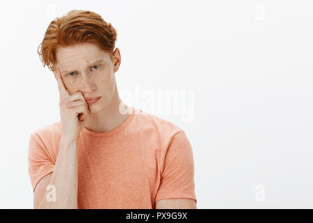 Cute ginger man trying to learn foreign language sitting intense and serious in class, cannot focus or understand anything, leaning on finger and frowning, staring seriously at camera Stock Photo