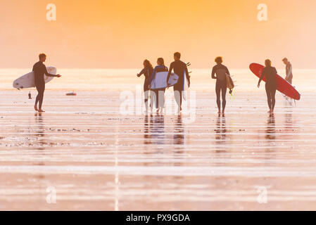 Surfing Newquay - A group of surfers carrying their surfboards and walking across Fistral Beach in late evening sunshine. Stock Photo