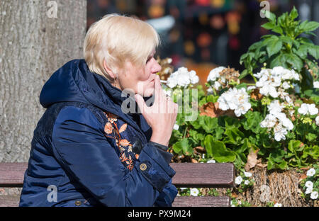 Side view of a middle aged Caucasian woman sitting smoking a roll-up cigarette in the UK. Stock Photo