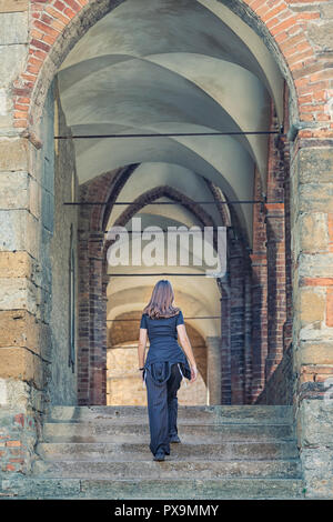 Young woman walks on away from camera up a set of medieval steep steps, Castell'Arquato, Piacenza, Italy Stock Photo