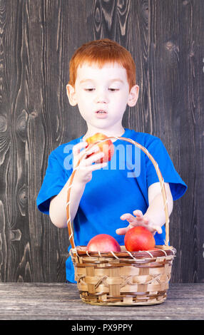 the boy looks at the nectarine, which is in his hand, there is a basket on the table with other nectarines and peaches Stock Photo