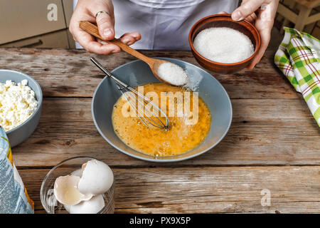 Male hands chef pours the flour into a plate on a wooden brown table in black utensils. Chef kneads the dough. Black background. The concept of cookin Stock Photo