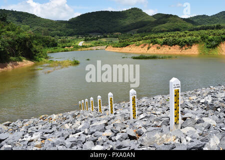 Small amount of water in the dam with mountain and blue sky and white cloud in background , Water level gauge or Staff Gauge with Thai alphabet letter Stock Photo